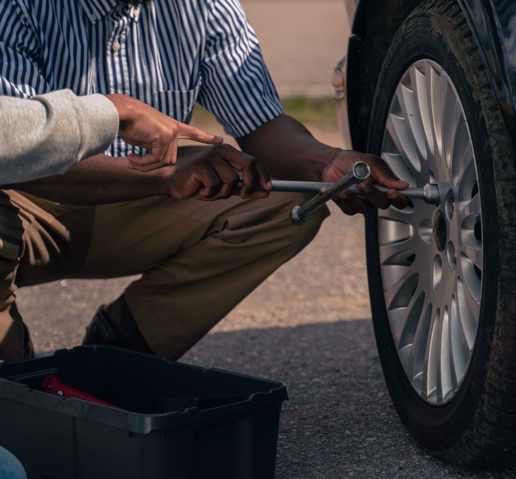 Two men collaborating to change a car tire on a sunny day.